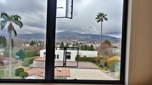 Une chambre avec une grande fenêtre donnant sur un paysage urbain, avec notamment un bâtiment moderne et des palmiers.