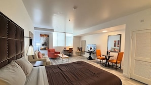Une chambre d’hôtel moderne dotée d’un grand lit, d’un bureau, d’une télévision et d’un coin salon avec des fauteuils et une table.