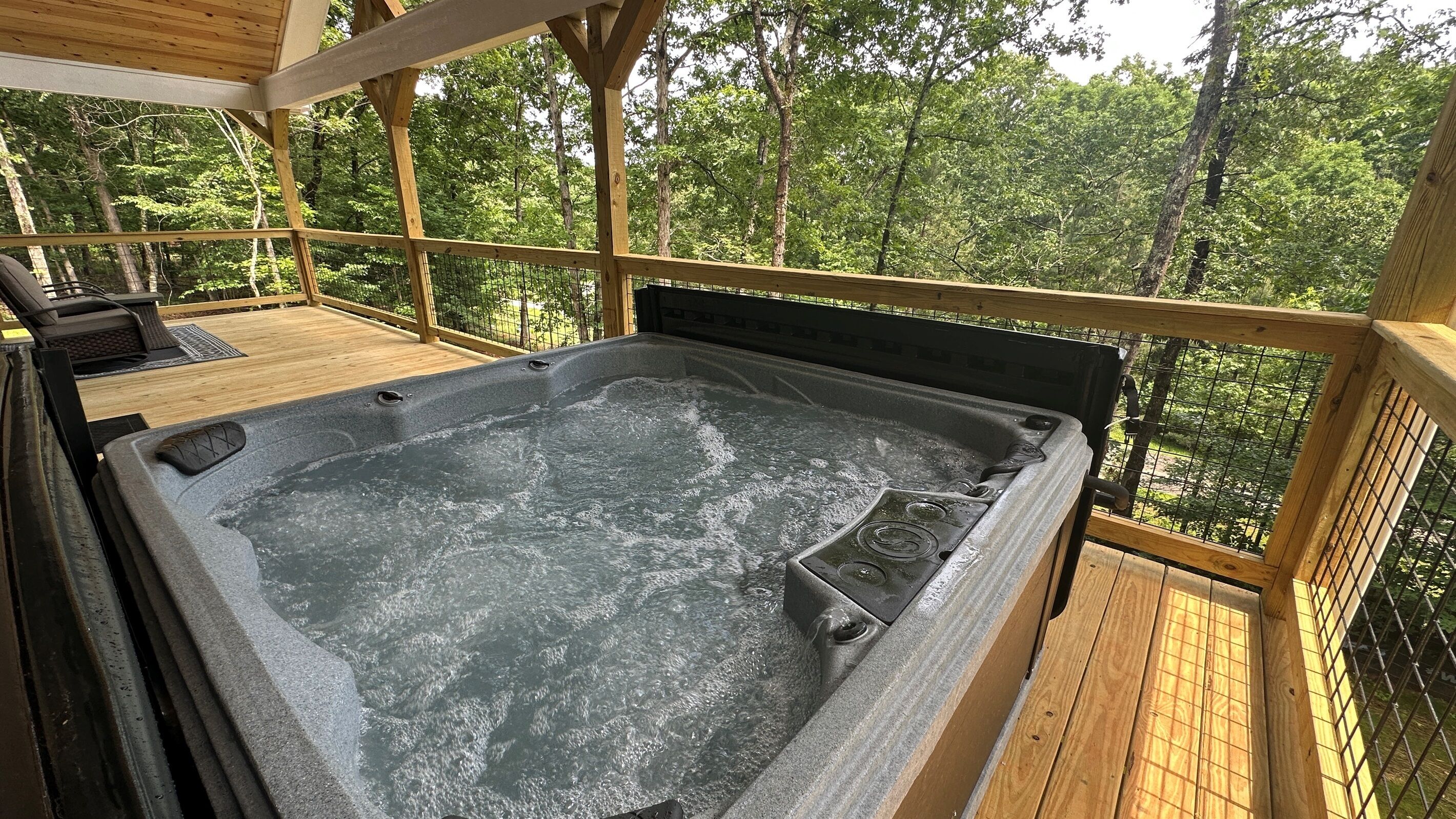 A hot tub on a wooden deck with a view of a forest.