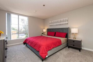 A bedroom with a bed, a nightstand, a dresser, and a window.
