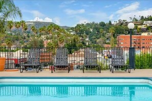 A pool area with lounge chairs and a view of a cityscape.