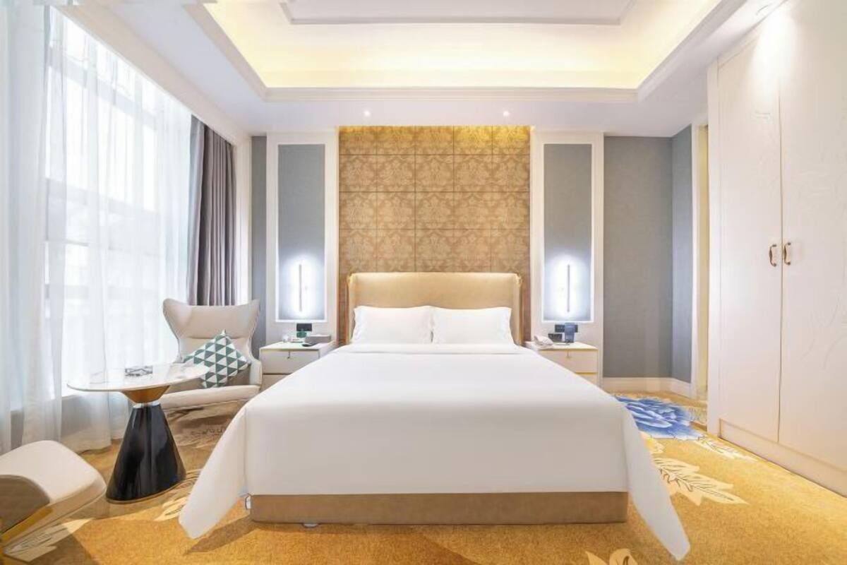 A hotel room with a large bed, bedside tables, a chair, a desk, and a wardrobe.