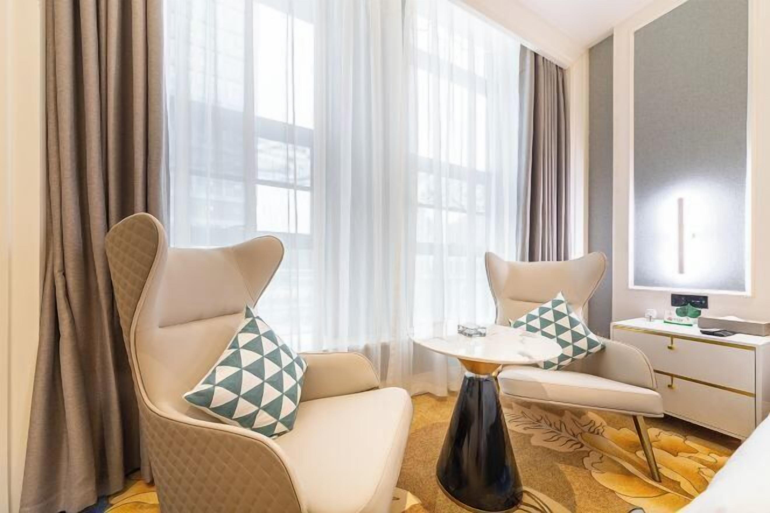 A hotel room with two armchairs, a small table, a bedside table, and a large mirror.