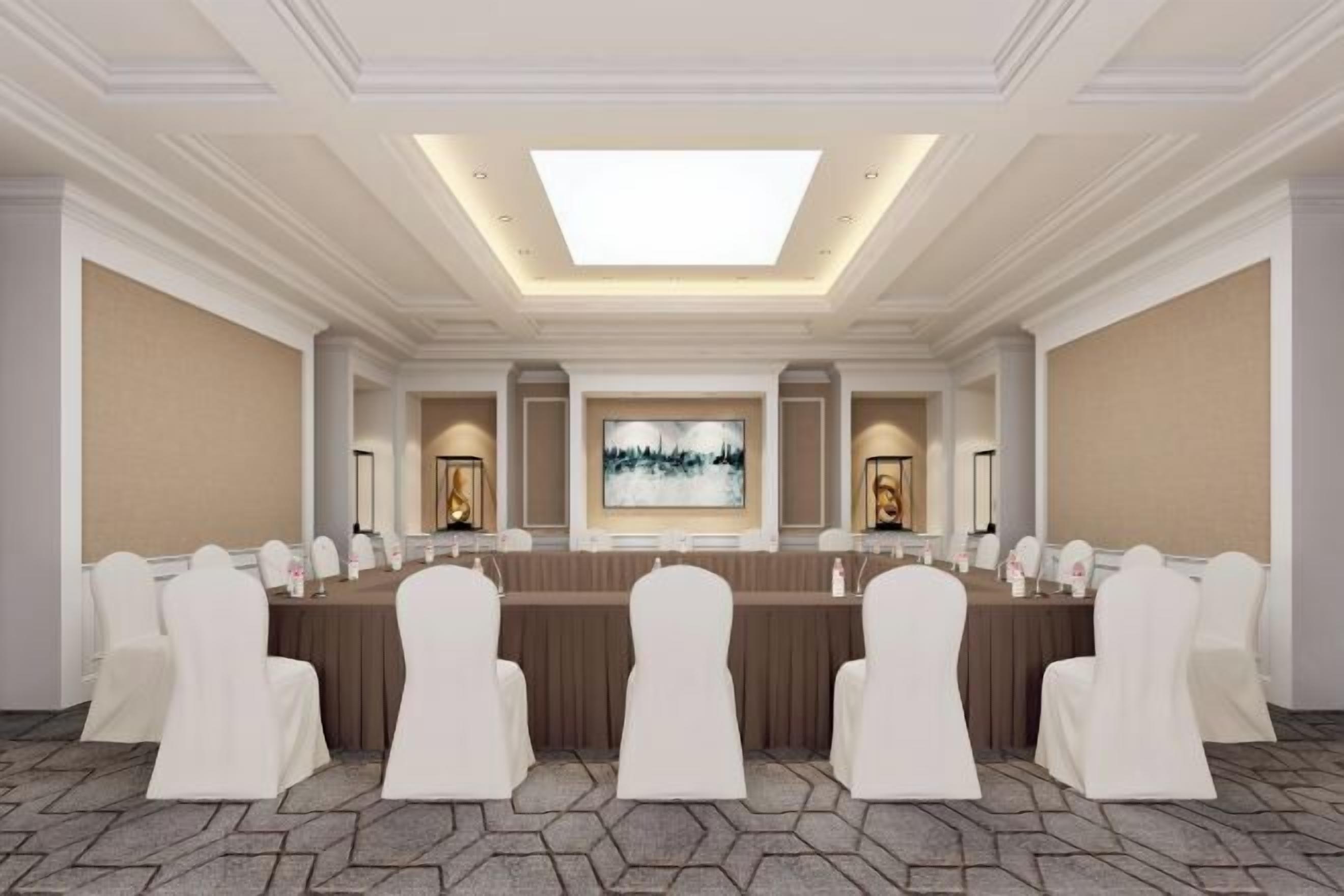 Une salle de conférence avec une longue table, des chaises blanches et un grand tableau accroché au mur.