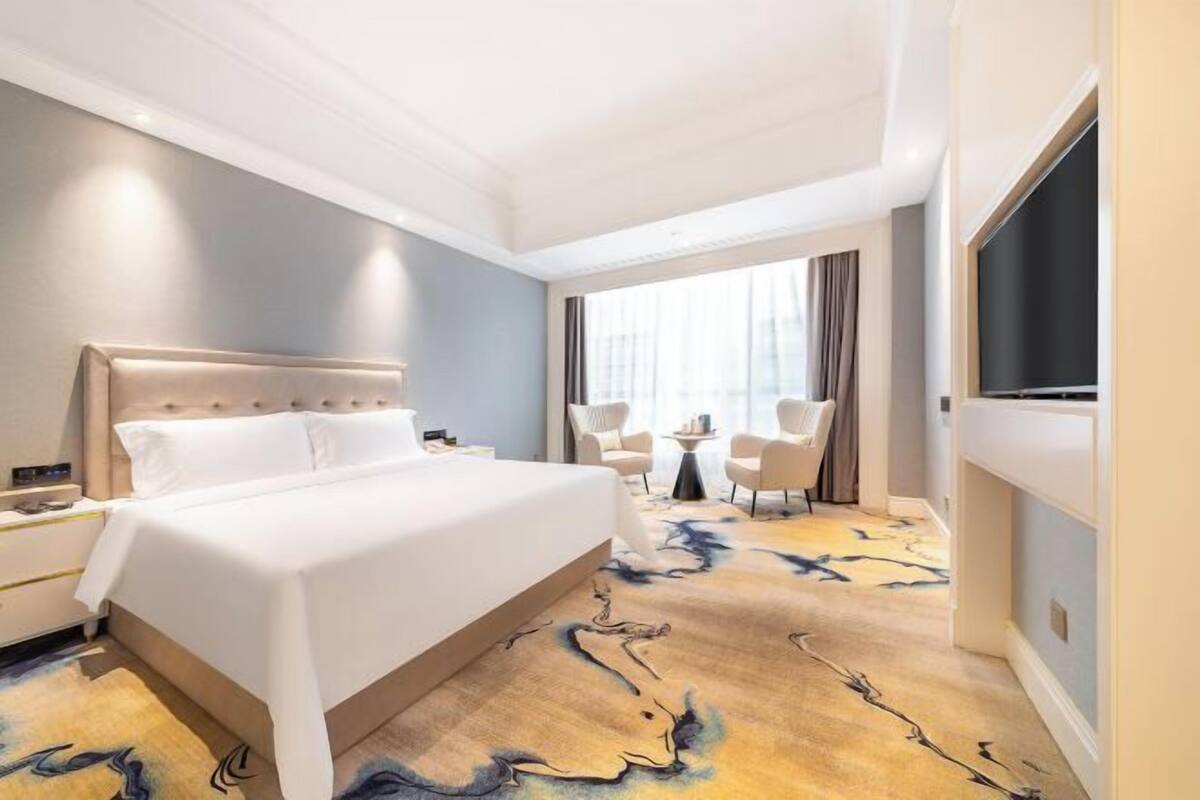 A hotel room with a large bed, a seating area with chairs, a small table, and a TV.