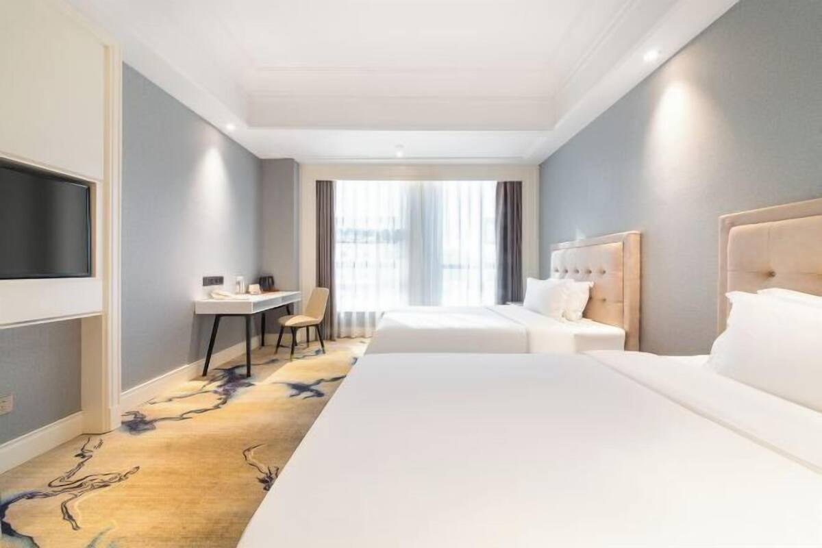 A hotel room with a bed, a desk, a chair, and a TV.