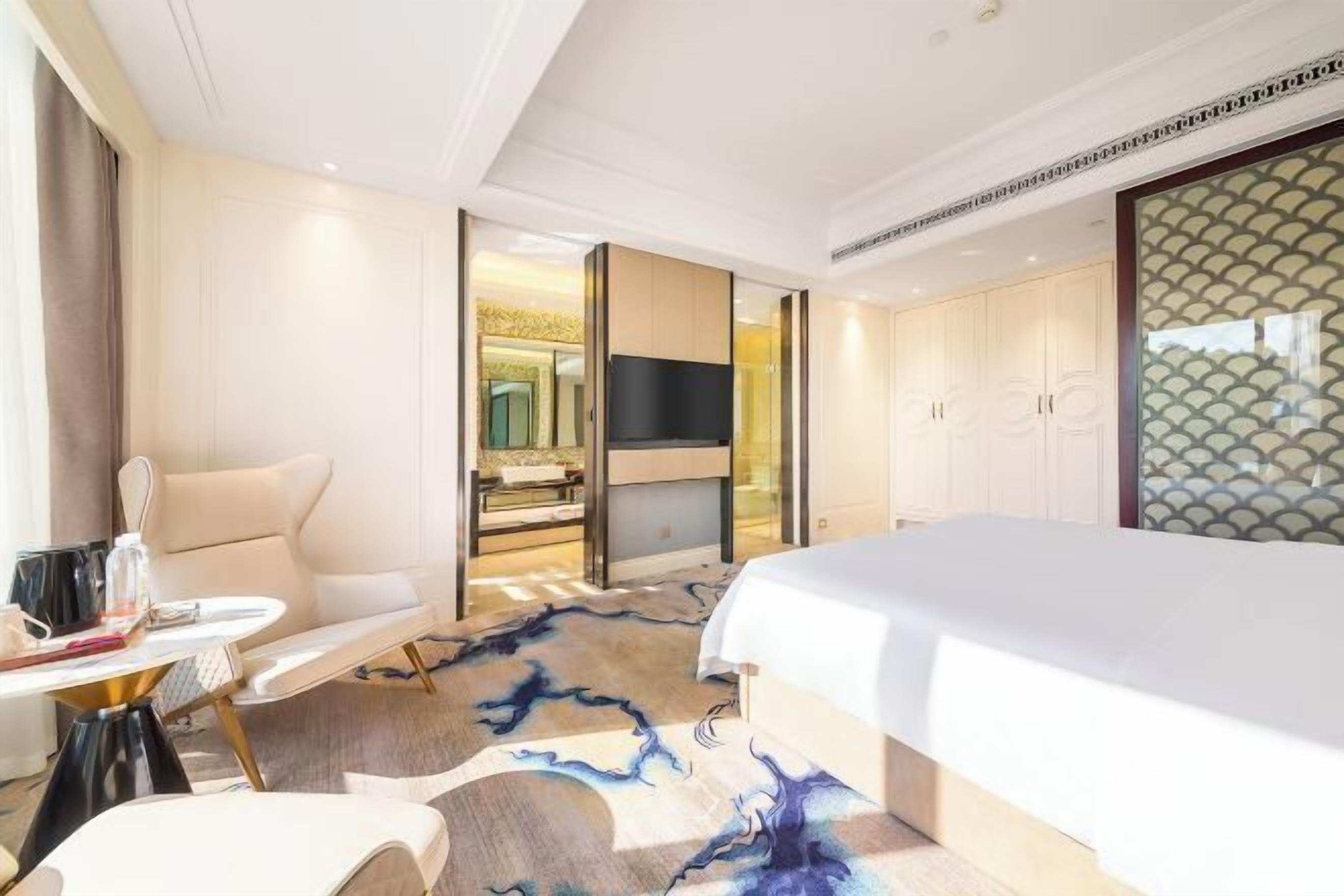 Habitación de hotel con cama, televisión, zona de estar y baño visible a través de una puerta abierta.