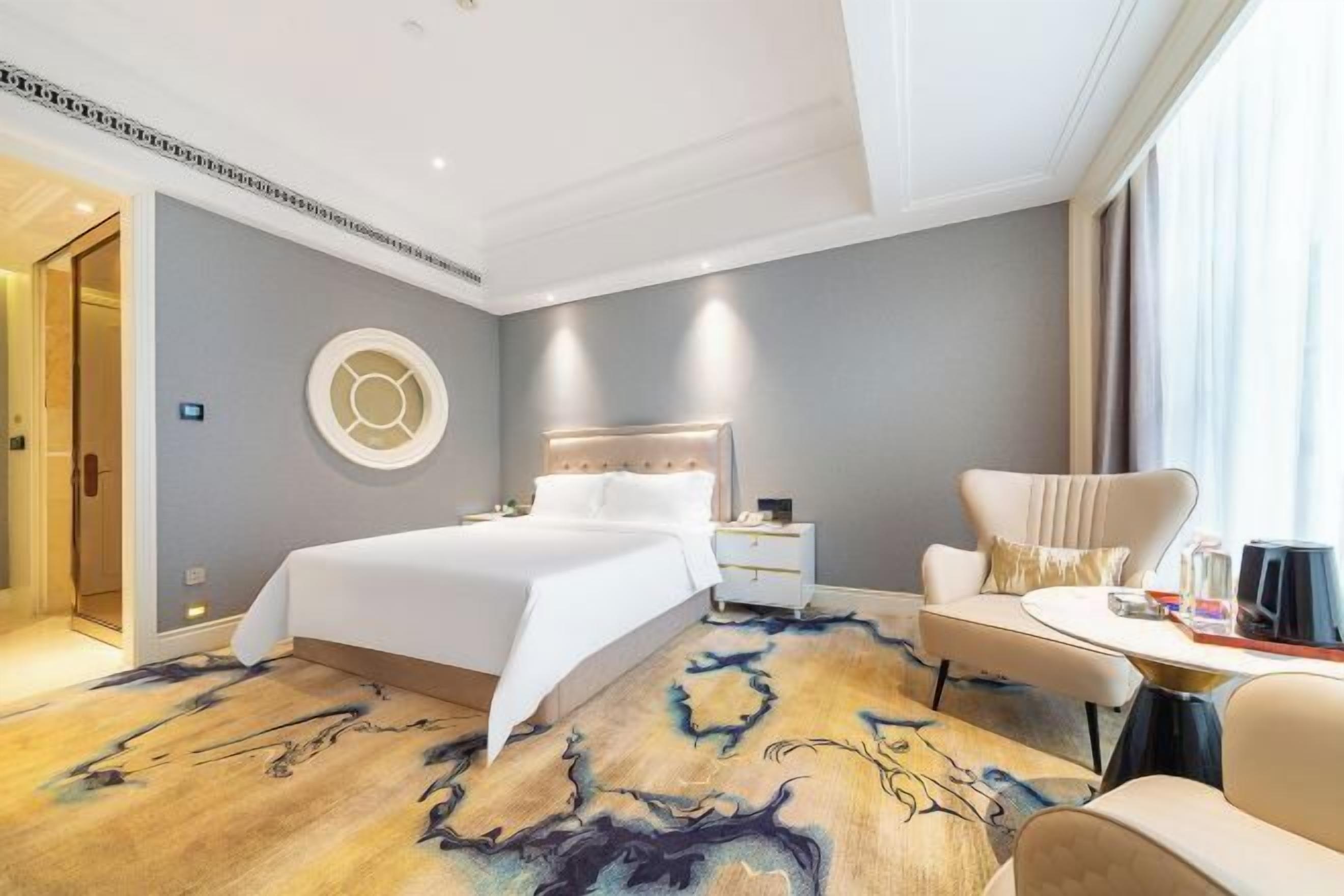 A modern hotel room with a large bed, a round wall decoration, a side table, and a sofa.