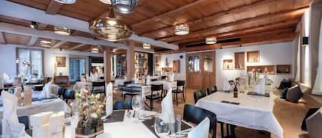 A spacious dining area with multiple tables, elegant lighting fixtures, and a wooden ceiling.