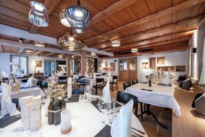 Un comedor amplio con varias mesas, luminarias elegantes y techo de madera.
