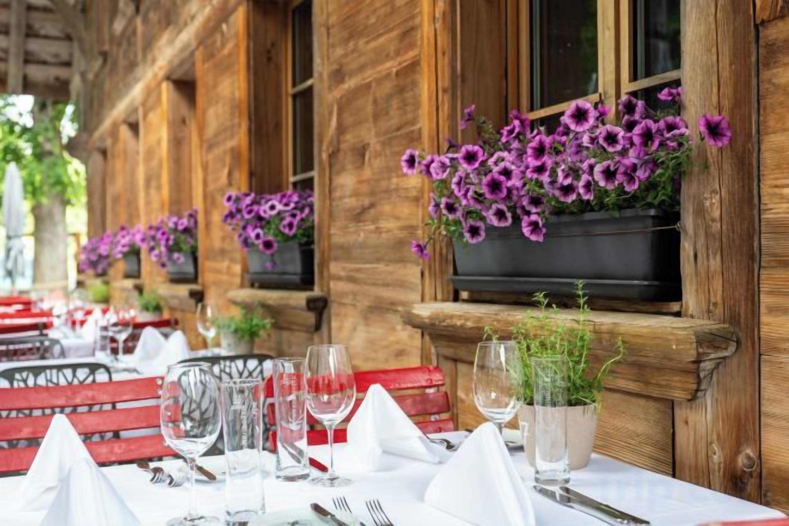 A restaurant with outdoor seating, tables set with white tablecloths, and purple flowers in hanging planters.