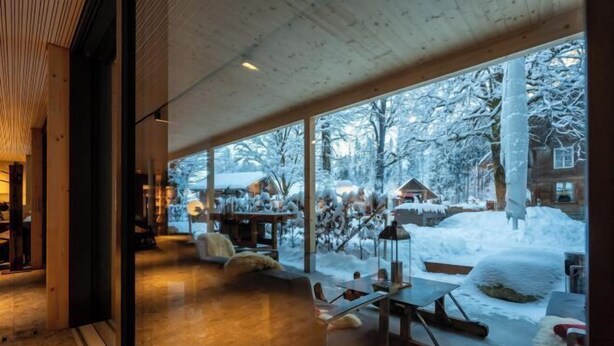Un interior moderno con ventanas amplias, techo de madera y vista a un área exterior nevada.