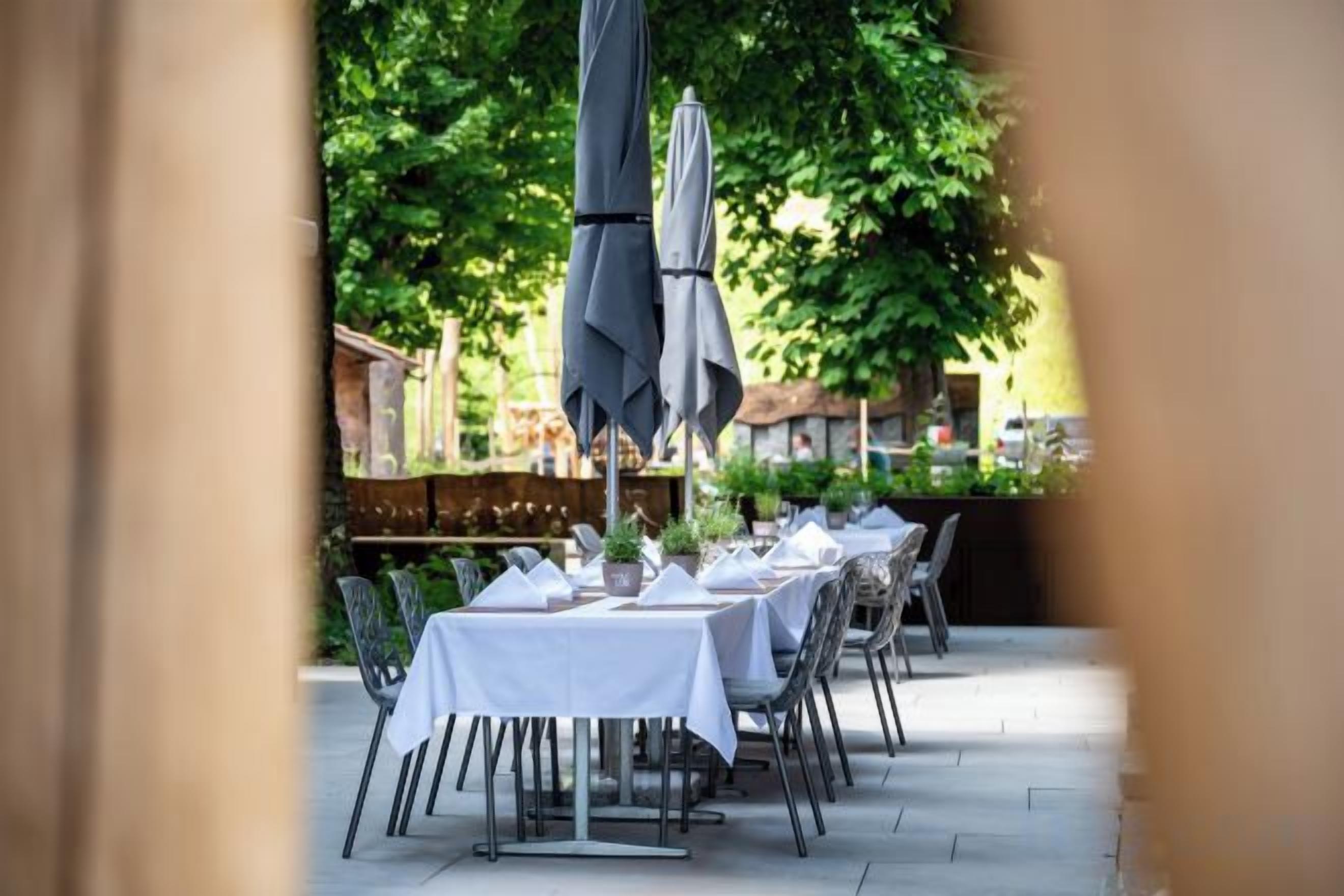 An outdoor dining area with tables and chairs, umbrellas, and a view of a building in the background.