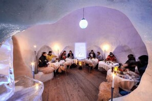 Un interior con forma de iglú, con mesas y sillas dispuestas para comer, una lámpara colgante y suelo de madera.