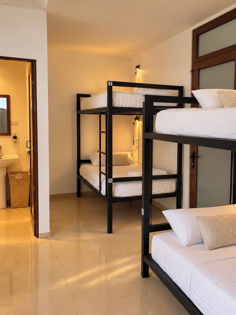Une chambre avec des lits superposés, un lavabo et une porte donnant sur une autre pièce.