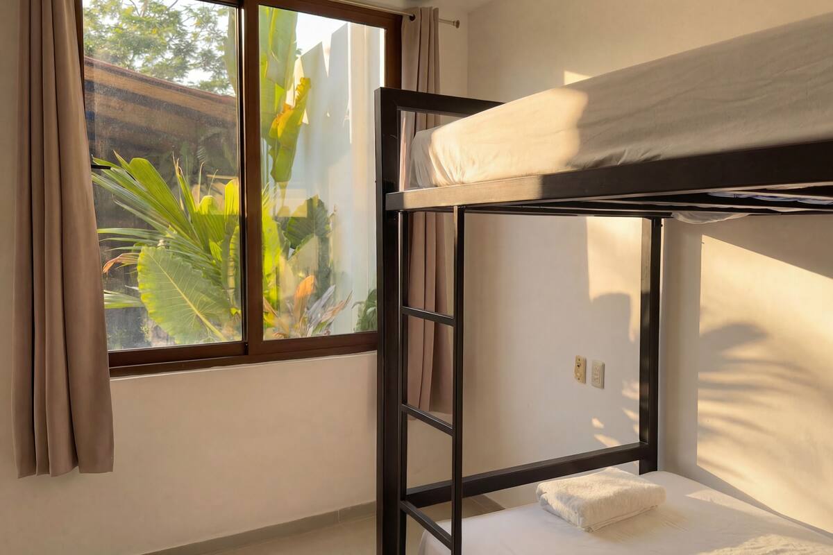A bunk bed room with a window, curtains, and a view of greenery.