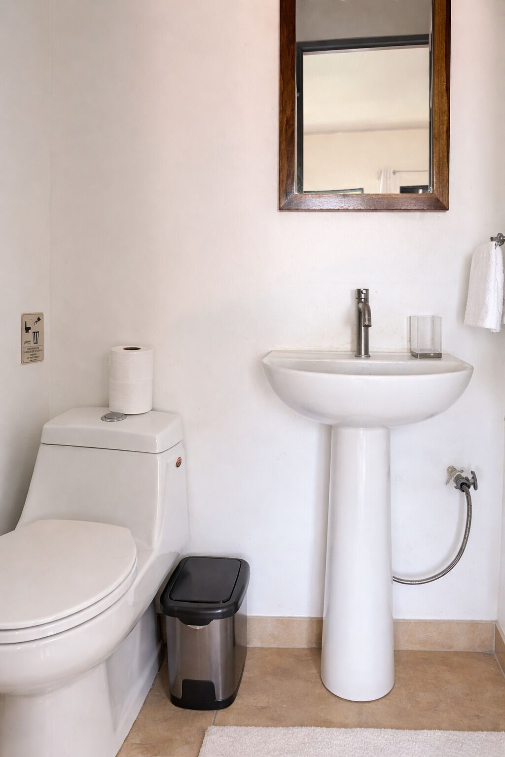 Une salle de bain équipée de toilettes, d’un lavabo, d’un miroir et d’une poubelle.