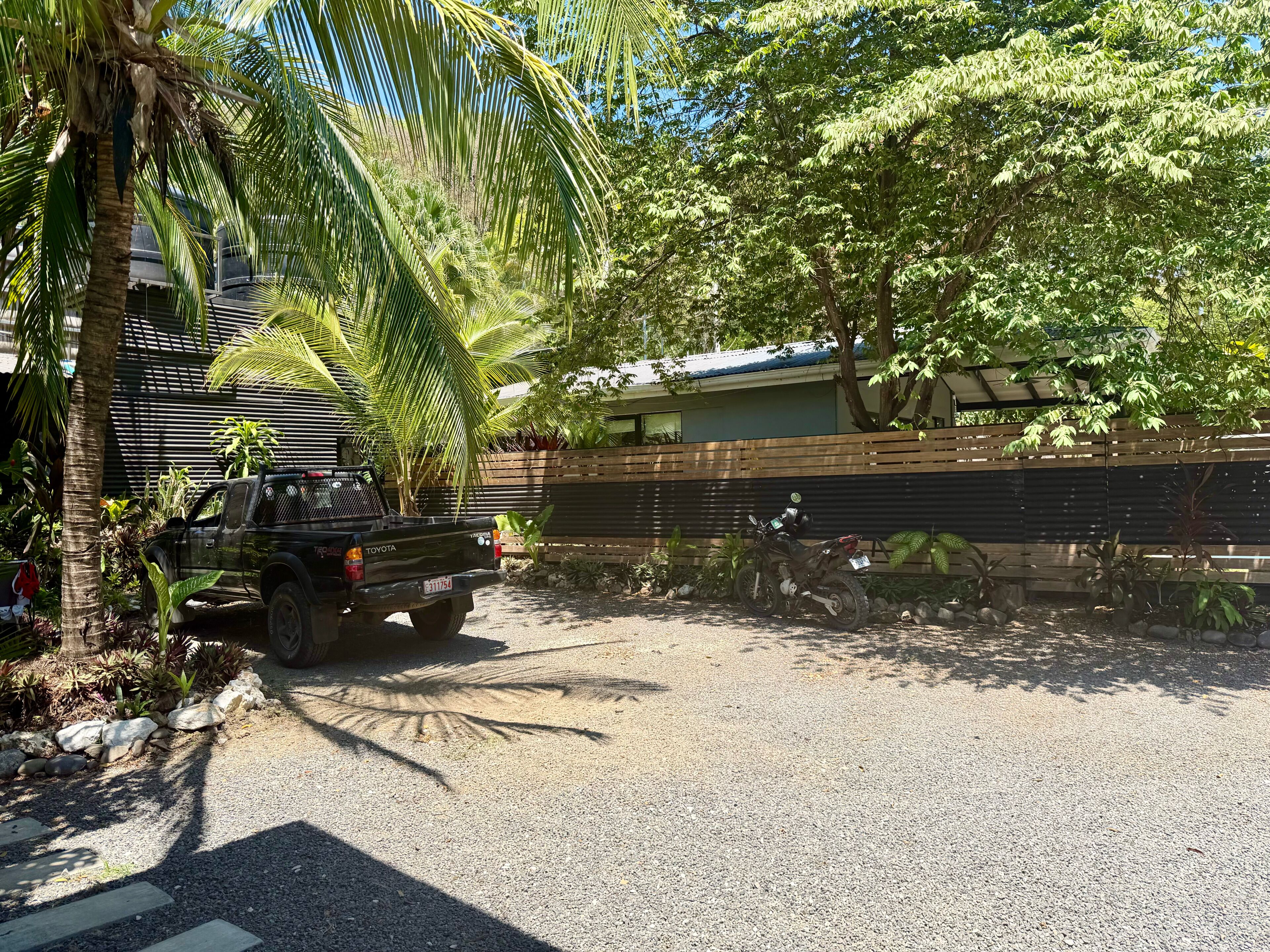 A black pickup truck parked in a gravel driveway, surrounded by lush greenery and a wooden fence.