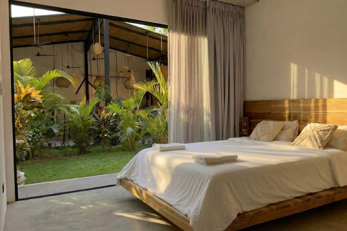 A bedroom with a bed, a view of a garden, and a wooden headboard.