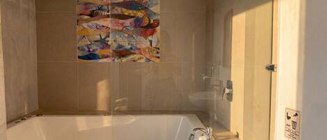 A bathroom with a bathtub, a toilet, and a shower. There is a colorful artwork on the wall.