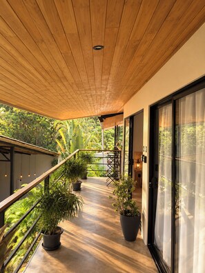 Un balcón techado con techo de madera, plantas en macetas y vistas al verdor.