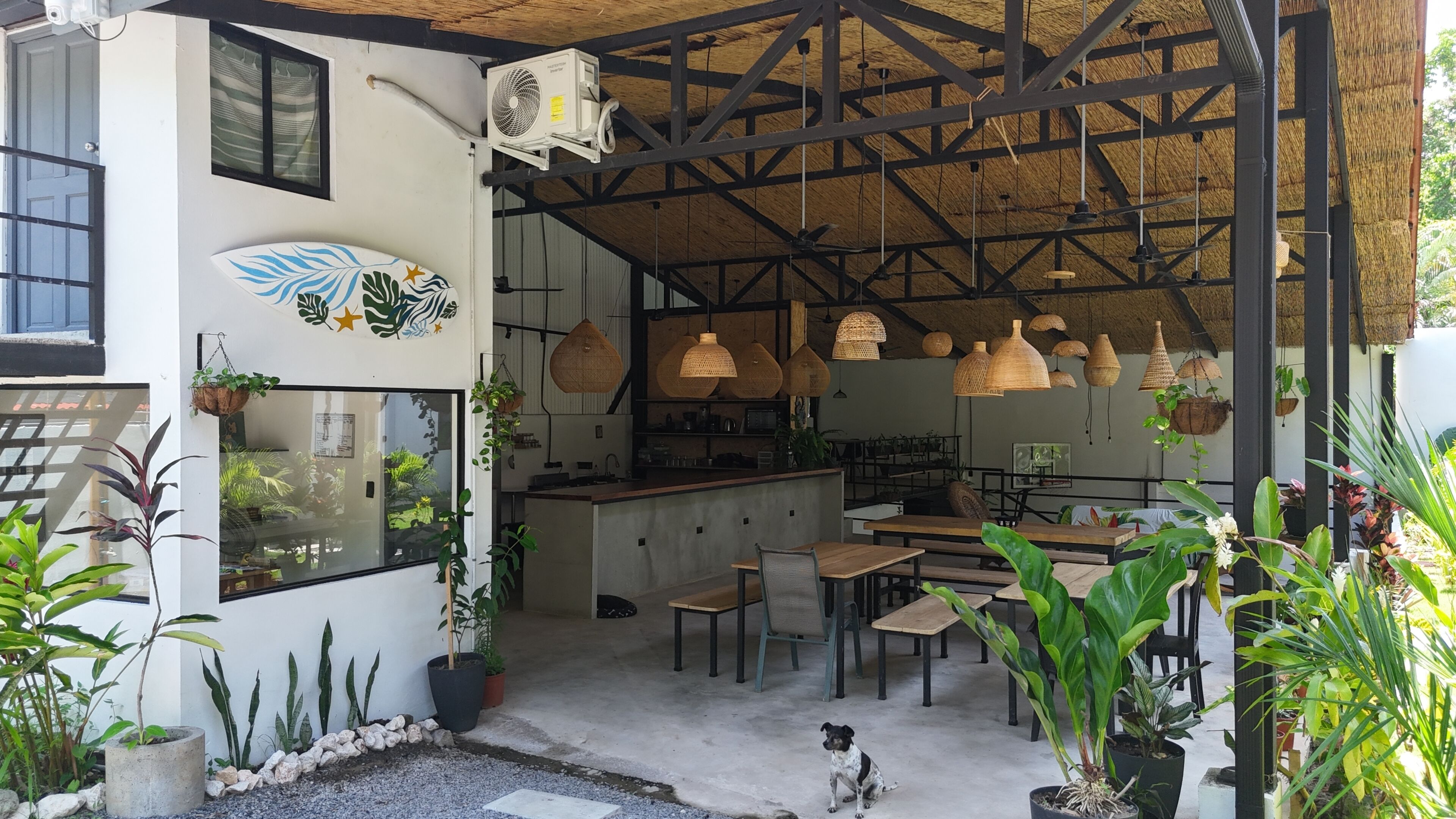 Uma área de refeições interna com mesas, cadeiras, luminárias pendentes e plantas em vasos.