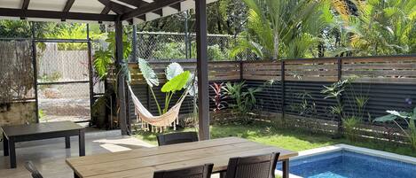 Ein überdachter Patio-Bereich mit Pool, Gartenmöbeln und einer Hängematte.