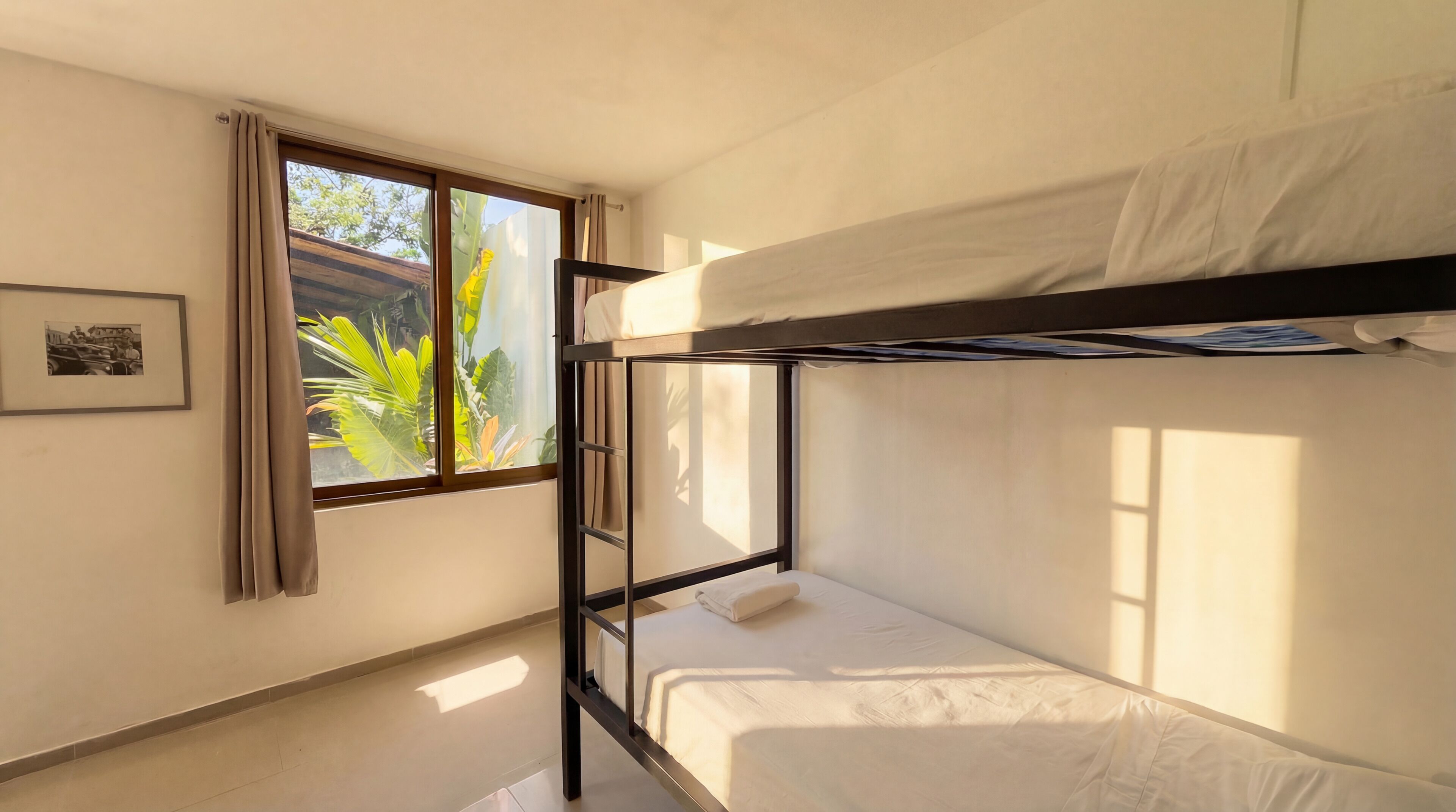 A bunk bed room with a window, curtains, and a framed picture on the wall.