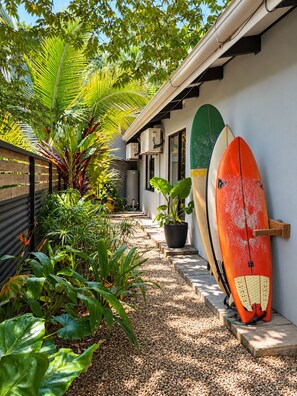 A pathway lined with potted plants leading to a building with surfboards leaning against the wall. - Aduana House (Cobano)