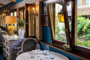 A dining area with a table set for two, a lamp, and a vase with flowers. - Hôtel Le Maréchal (Colmar)