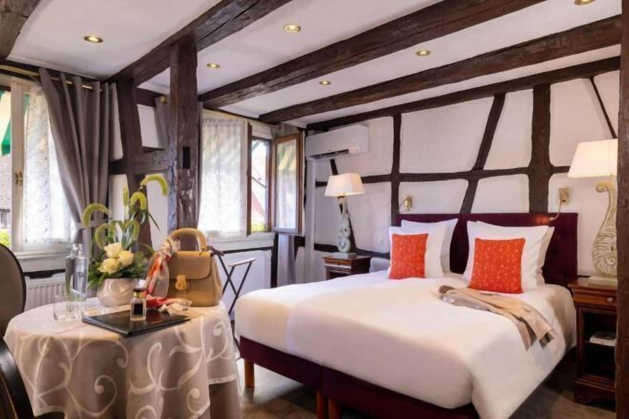 Une chambre d’hôtel avec un grand lit, un bureau avec une chaise, une table avec un vase de fleurs et une fenêtre avec des rideaux.