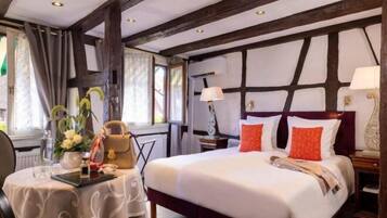 Habitación de hotel con una cama grande, un escritorio con silla, una mesa con un florero y una ventana con cortinas.