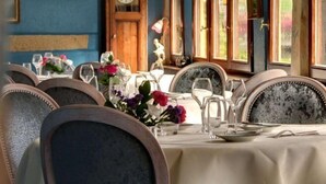 A dining table set with chairs, a clock, and a window with curtains. - Hostellerie le Marechal Colmar (Colmar)