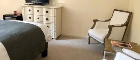 Habitación de hotel con una cama, un televisor en una cómoda, una silla y una mesita con una revista.