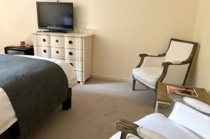 Habitación de hotel con una cama, un televisor en una cómoda, una silla y una mesita con una revista.