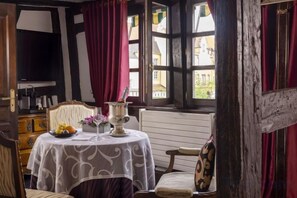 A room with a table set for dining, a television, and a window with curtains. - Hôtel Le Maréchal (Colmar)
