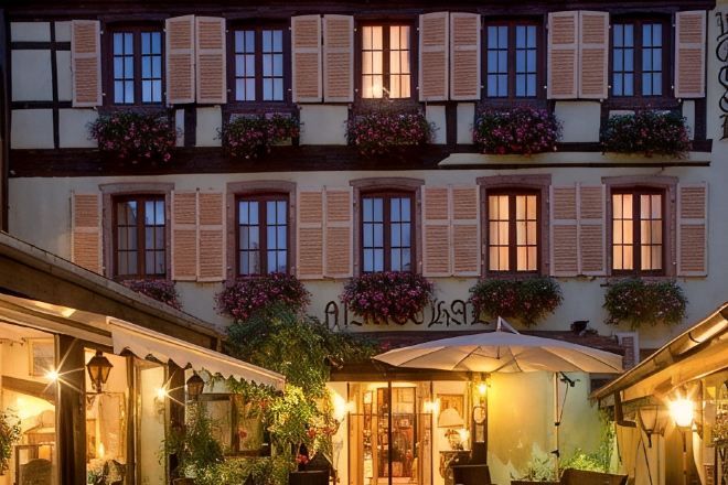 Un hotel con varias ventanas, algunas con contraventanas, y un letrero sobre la entrada.