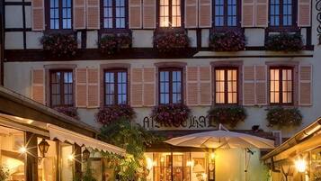 Un hotel con varias ventanas, algunas con contraventanas, y un letrero sobre la entrada.
