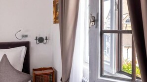 A room with a bed, a nightstand, a window with curtains, and a radiator. - Hostellerie le Marechal Colmar (Colmar)