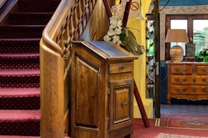 A wooden cabinet with drawers, a staircase with a wooden handrail, and a patterned rug on the floor. - Hôtel Le Maréchal (Colmar)