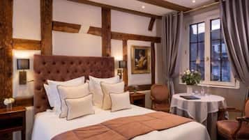 A bedroom with a large bed, a wooden headboard, a round table with a chair, and a window with curtains.