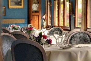 A dining area with tables set for four, chairs with cushioned backs, and a clock on the wall. - Hôtel Le Maréchal (Colmar)