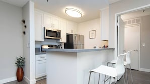 A modern kitchen with white cabinets, stainless steel appliances, and a central island with bar stools.