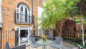 A patio with a glass table and chairs, a barbecue grill, and a small seating area with a sofa and cushions.