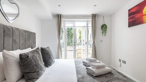A bedroom with a bed, pillows, a heart-shaped mirror, a painting, and a view of the outdoors.