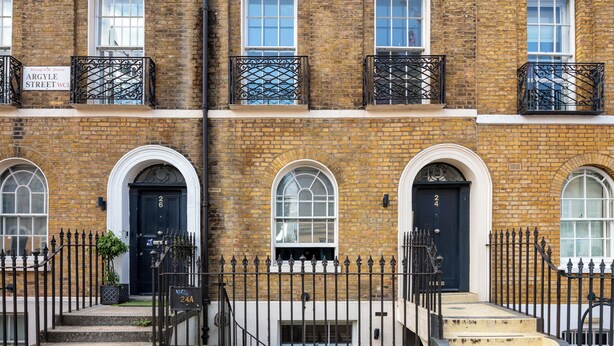 A brick building with three black doors, each with a white arch above. There is a black wrought iron fence in front.