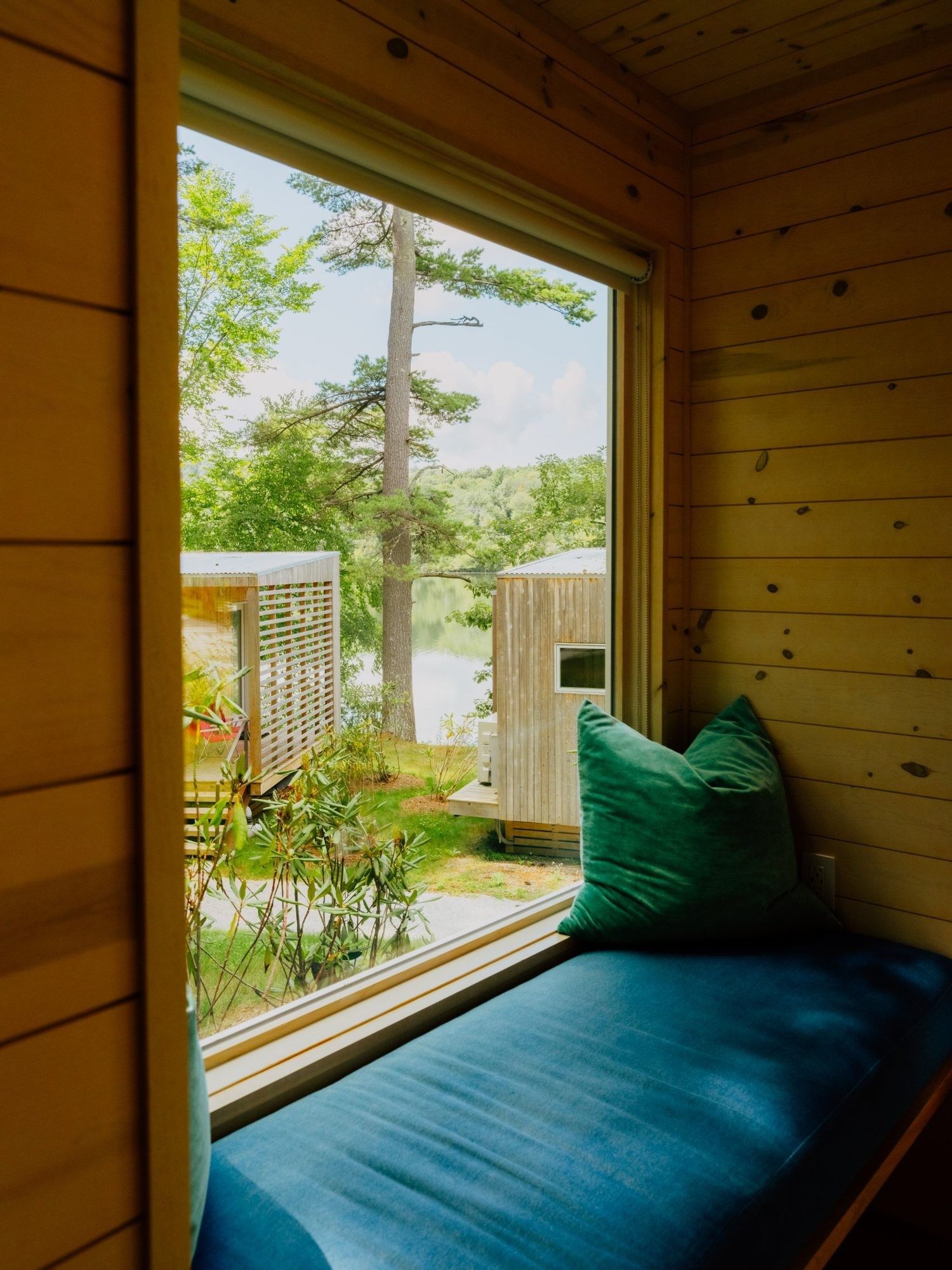 A wooden cabin with a window seat overlooking a pond and trees.