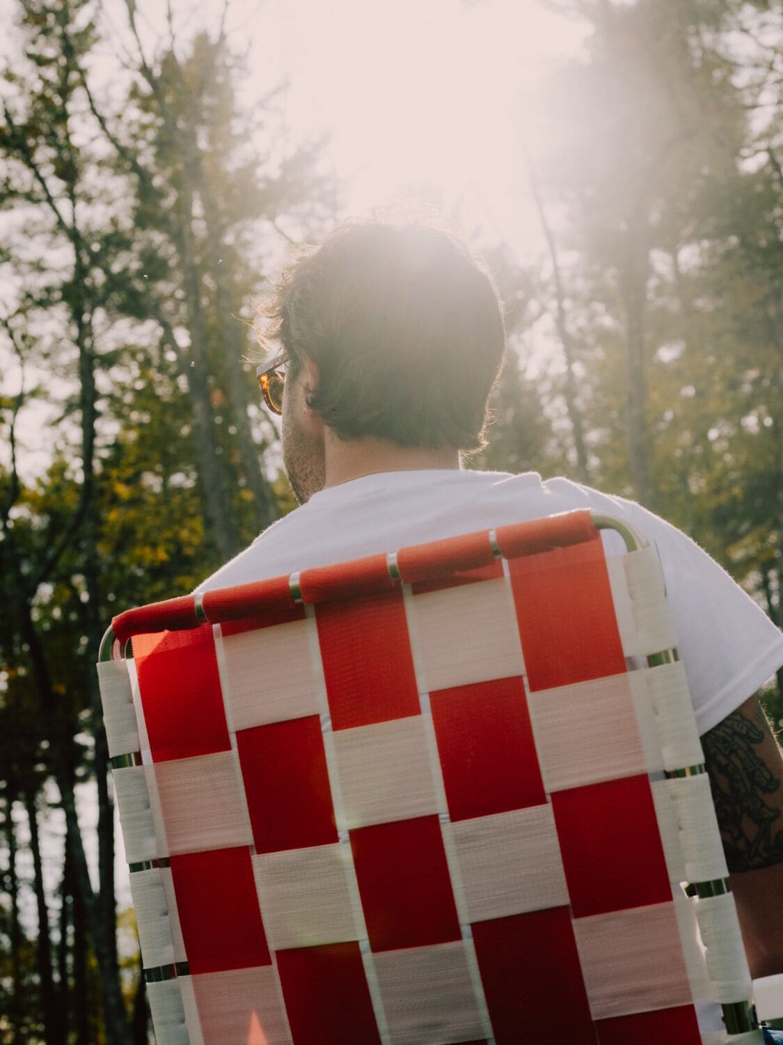A person seated in a red and white checkered chair outdoors, with trees in the background.