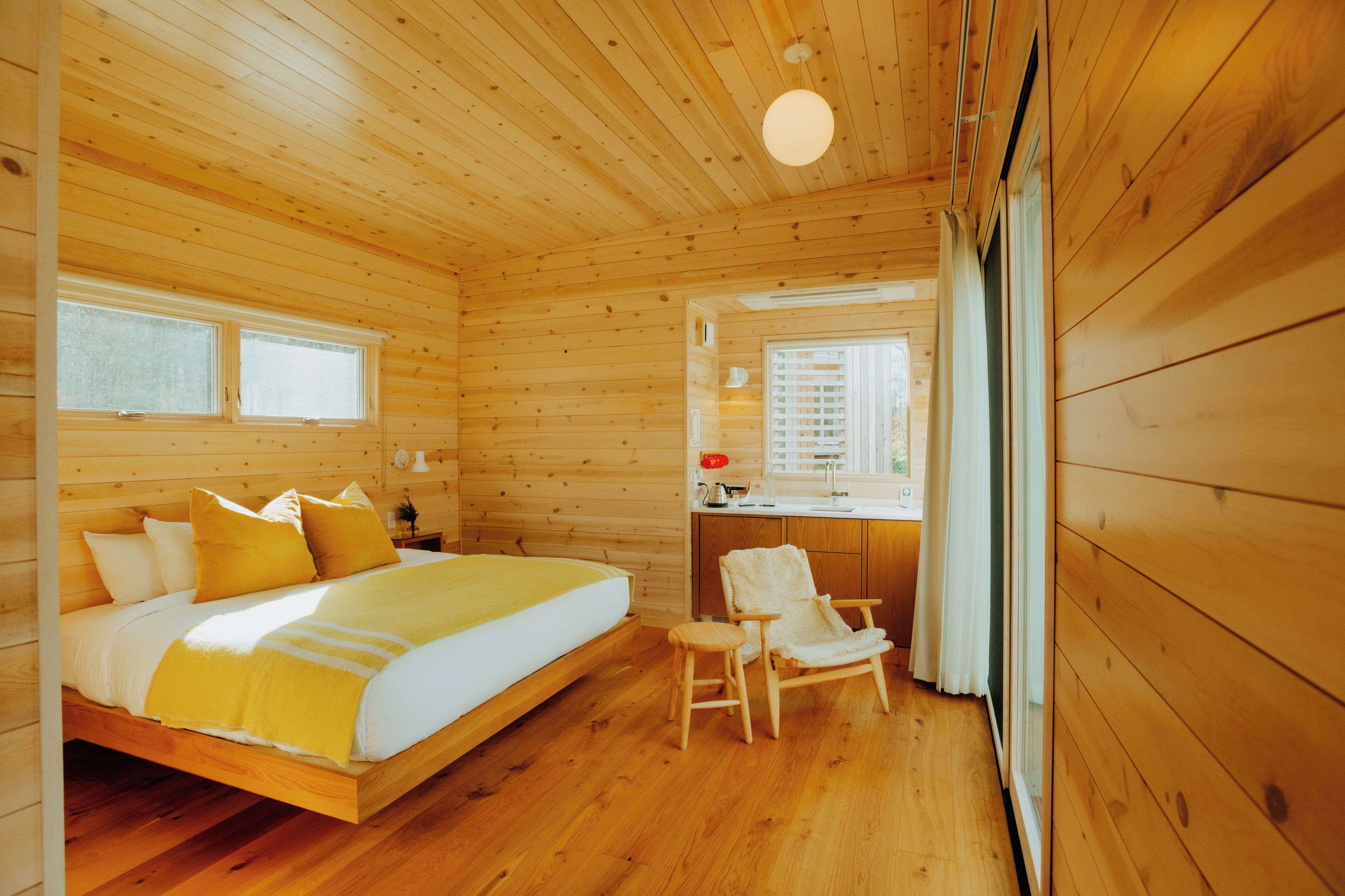 A wooden cabin with a bed, a chair, a desk, and a window.