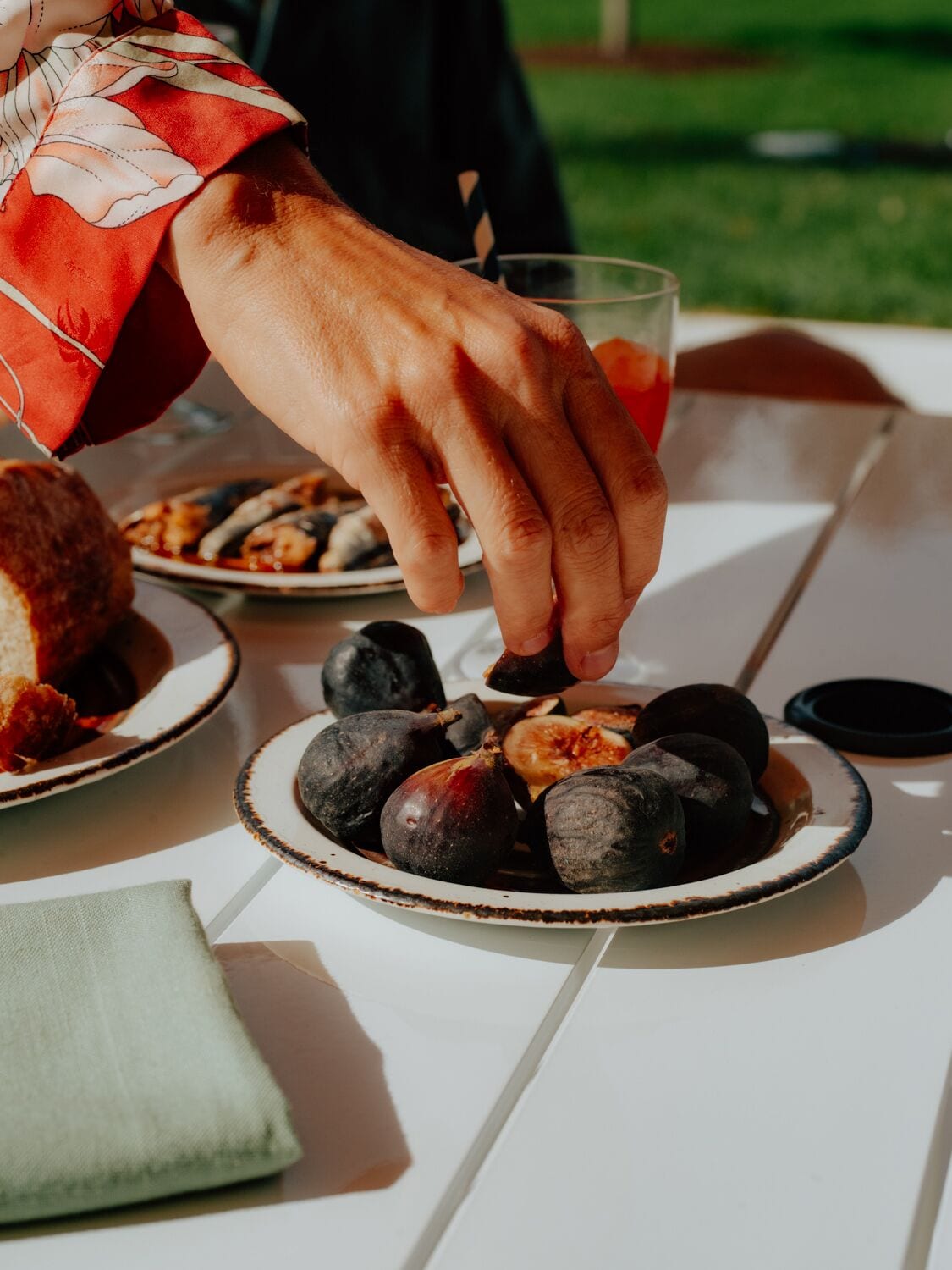 A person serving figs on a white table with a glass of drink and bread.